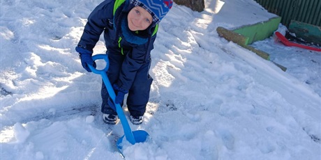 Powiększ grafikę: Chłopiec w zimowym stroju łopatą odgarnia śnieg w ogrodzie przedszkolnym