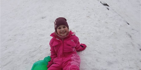 Powiększ grafikę: Dziewczyna siedzi na śniegu trzymając sanki. Uśmiecha się
